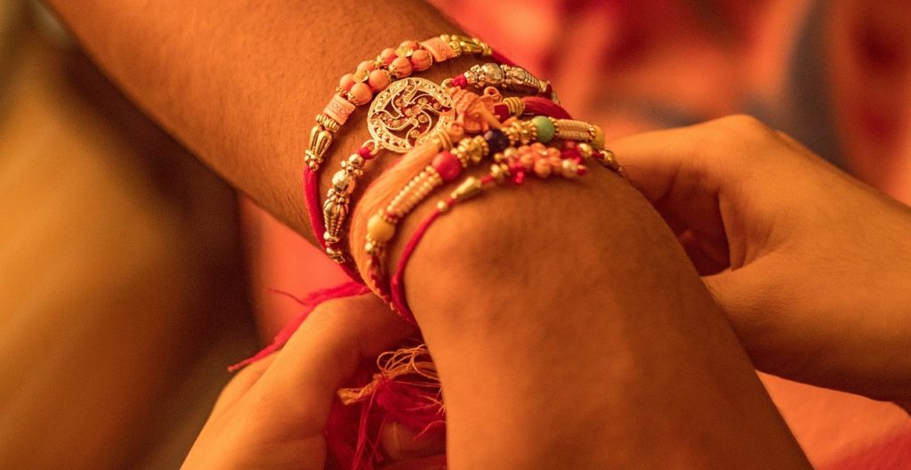 Shows sister tying a ceremonial Rakhi on her brother's wrist during Raksha Bandhan 